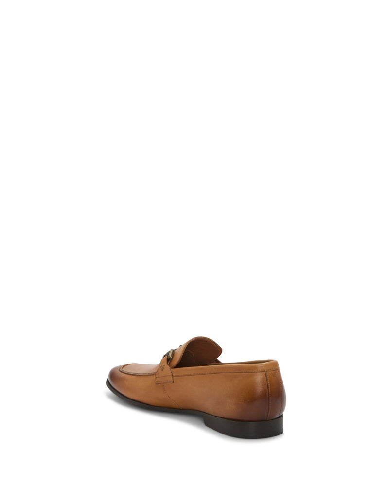 The Vince Camuto Men's Sevvano Dress Loafer is shown from a rear-side angle against a white background, featuring tan leather, a sleek slip-on design, low black heel, and an elegant strap detail across the upper.
