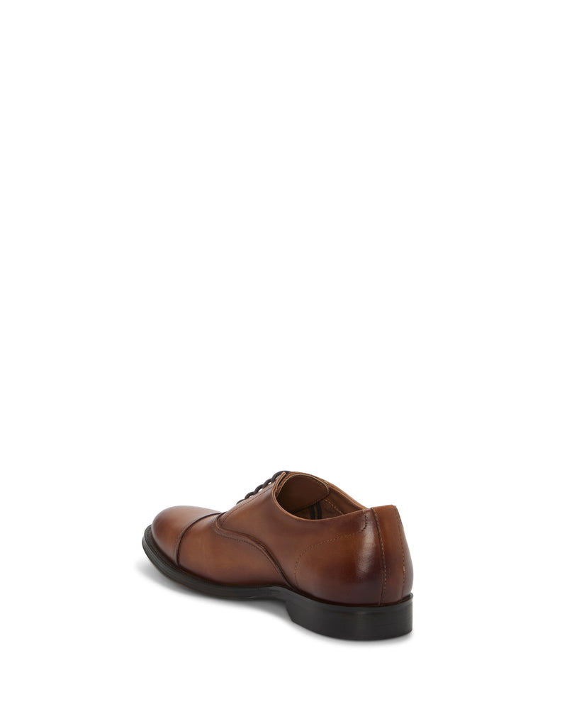 The Vince Camuto Men's Urii Dress Oxford, a brown leather cap toe shoe, is displayed at an angle from the back right side against a white background.