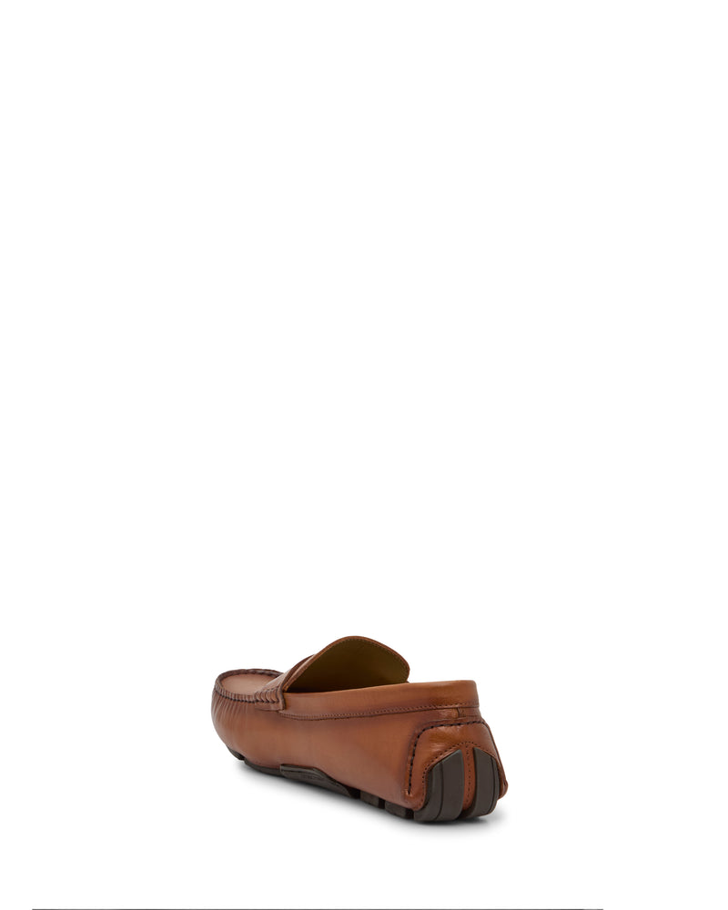 The Vince Camuto Men's Vitzroy Slip-On is shown from the back at an angle, showcasing its brown leather, stitched accents, and rubber sole. The versatile loafer silhouette stands out against a plain white background.