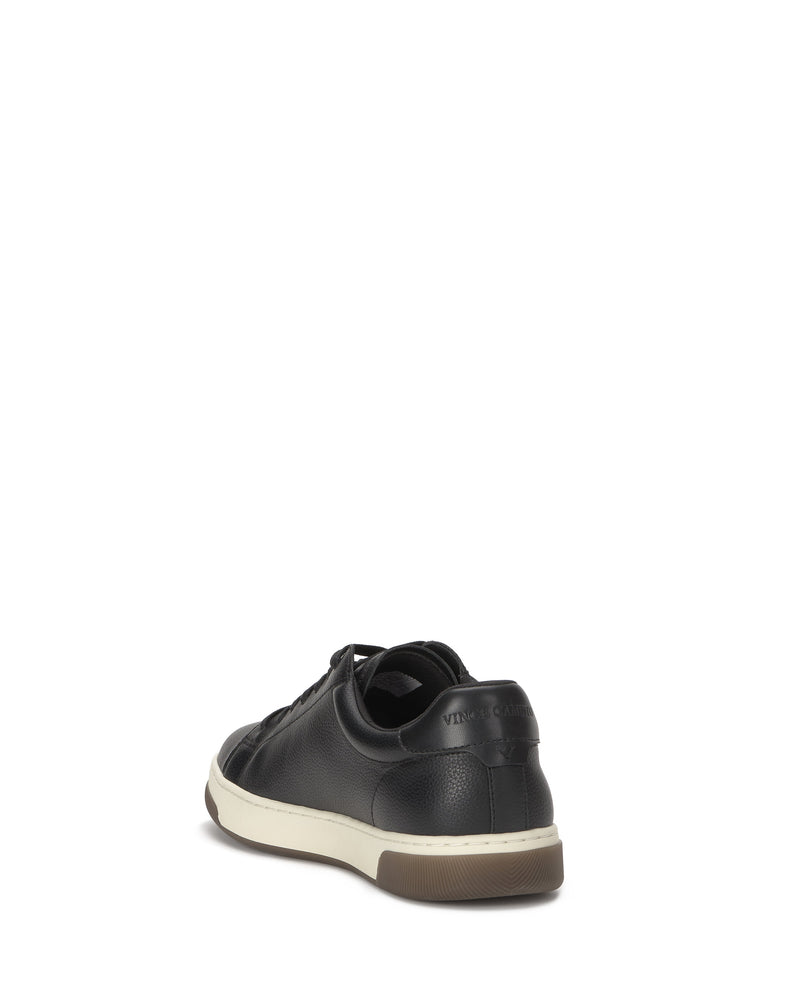 The Vince Camuto Men's Wynsten Sneaker is shown in black with a white sole, viewed from the back right against a white background. The visible heel patch and textured rubber outsole highlight its casual look and comfortable EVA insole.