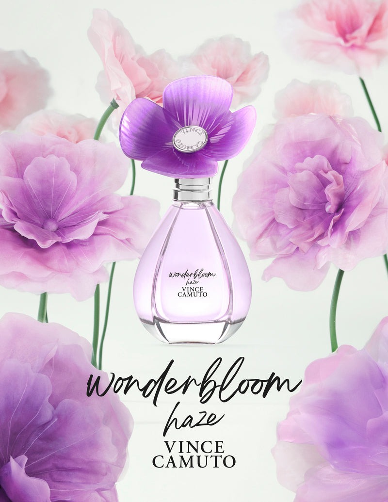 The Vince Camuto Wonderbloom Haze 3.4 oz Eau de Parfum Spray features a purple flower-shaped cap and sits among soft pink and purple flowers, evoking dreamy notes of warm amber and Madagascar vanilla.