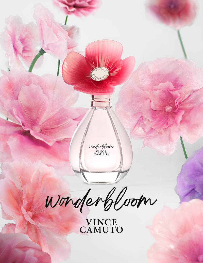 A clear Wonderbloom 3.4 oz Eau de Parfum Spray bottle by Vince Camuto, with a pink flower cap, is surrounded by pastel flowers and white freesia. "Wonderbloom" appears in script below the bottle.