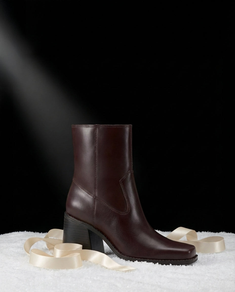 Burgundy Sybren bootie with cream satin ribbon spooled around the base, resting on snow against a dark background