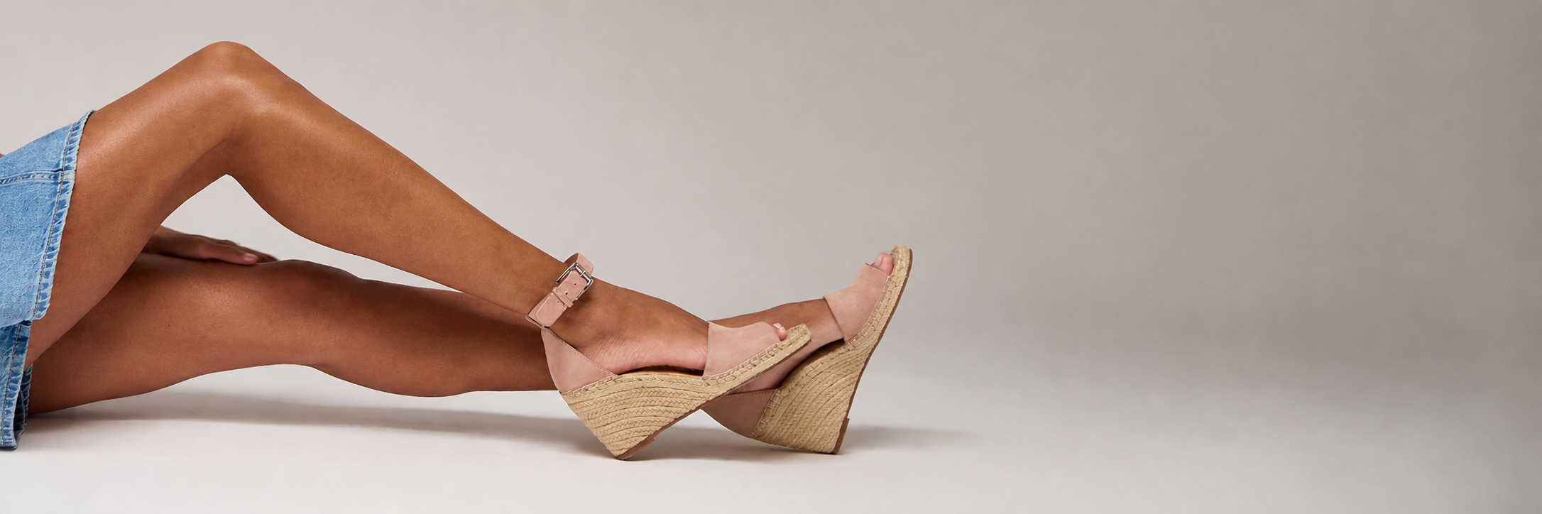 Woman laying in gray studio setting in jean skrit and peach espadrille sandals, only shown from waist down.