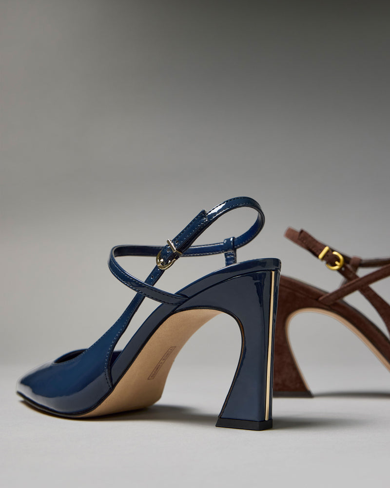 A pair of Vince Camuto Bevarin Pumps are side by side: a glossy navy slingback with a patent heel and pointed toe is in the foreground, while a brown suede slingback sits in the background; both feature chunky, curved heels.