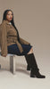 Women on a tan back ground wearing Fall boots sitting on a bench 